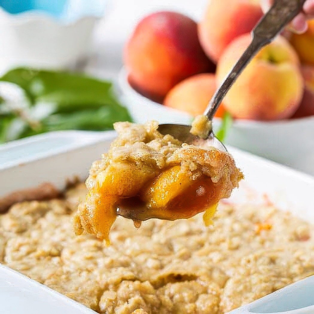 Spoon scooping Oatmeal Cookie Peach Cobbler out of a baking dish.