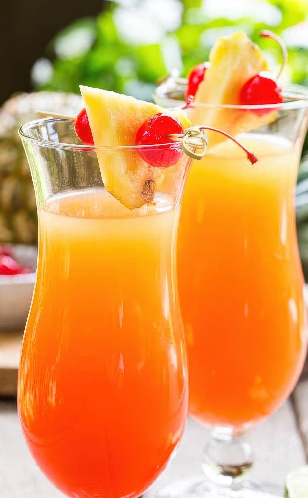 Two cocktails garnished with cherries and pineapple.