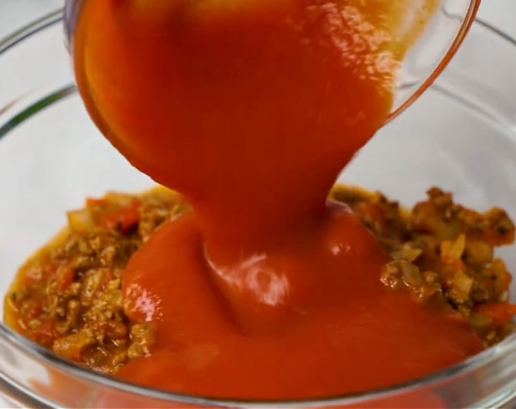 Adding tomato sauce to ground beef mixture.