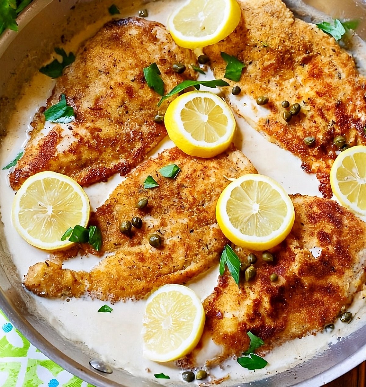 Creamy Chicken Piccata in pan with lemon slices.