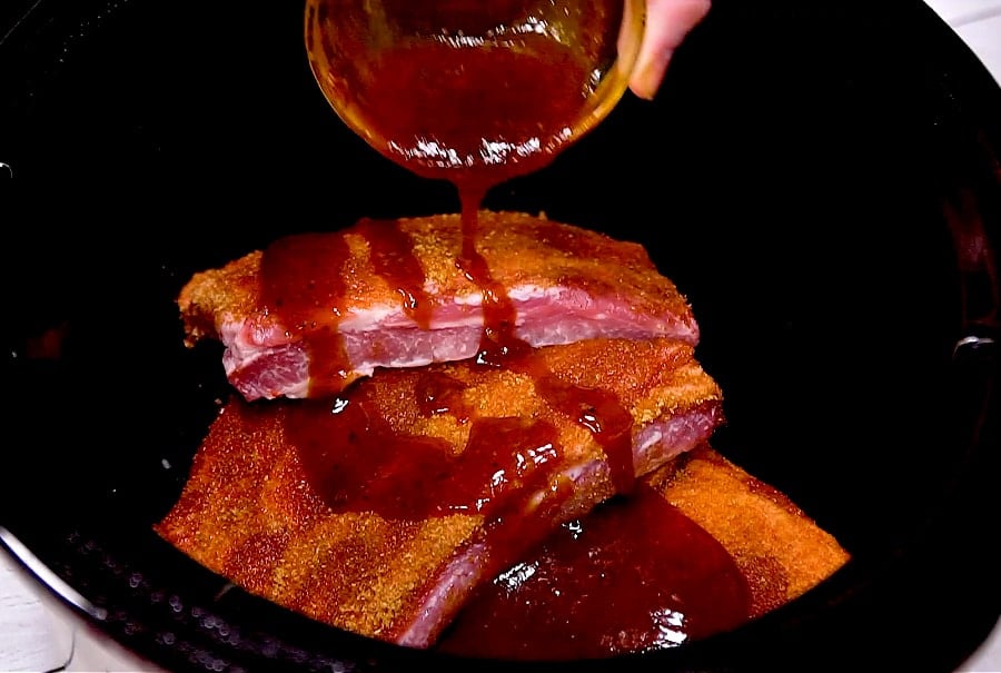 Pouring sauce over ribs in slow cooker.