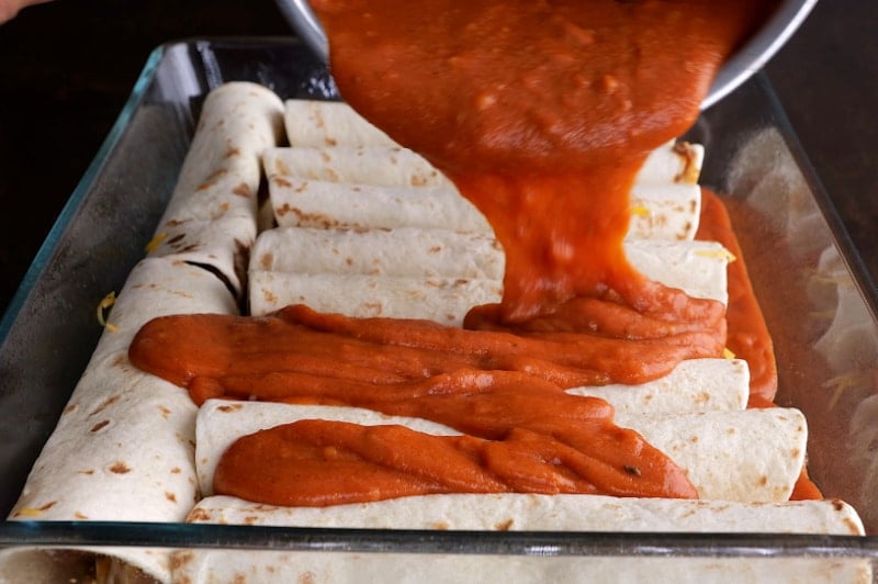 Pouring sauce over the enchiladas.