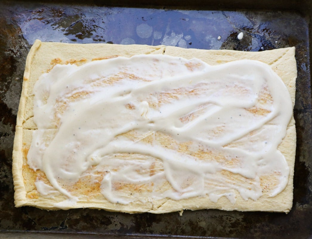 Alfredo sauce spread on crescent dough.