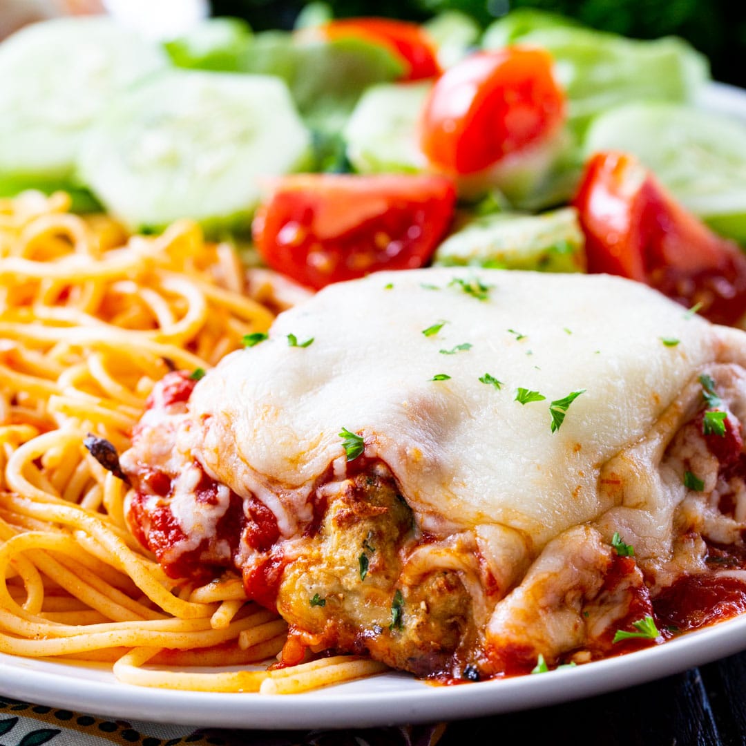 Chicken Patty Parmesan on a plate with spaghetti and salad.