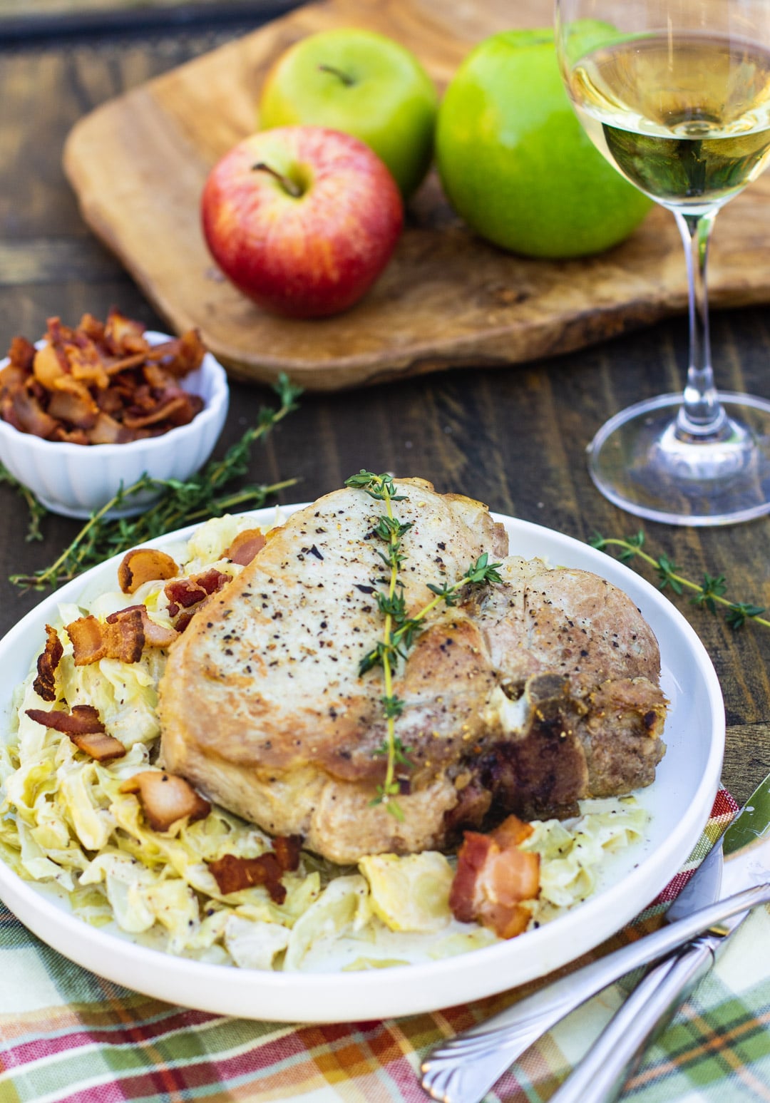 Pork Chop over cabbage on a plate with apples and glass of wine in background.