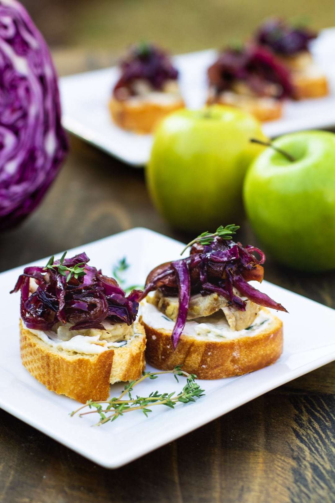 Pork Crostini on a plate with red cabbage and apples in background.