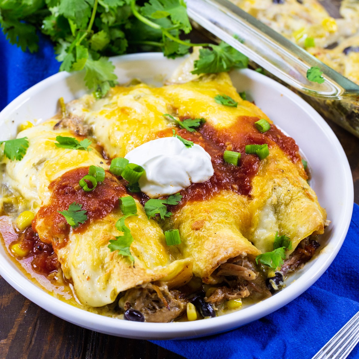 Three Pulled Pork Enchiladas topped with sour cream on a plate.