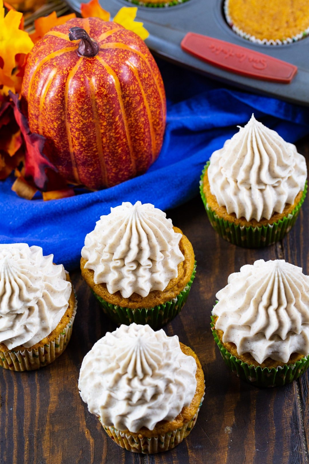 Pumpkin Cupcakes with Cinnamon Cream Cheese Frosting on tabletop with pumpkin.