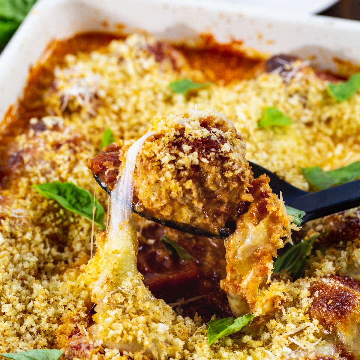 Spoon scooping a Chicken Parmesan Meatballs out of a baking dish.