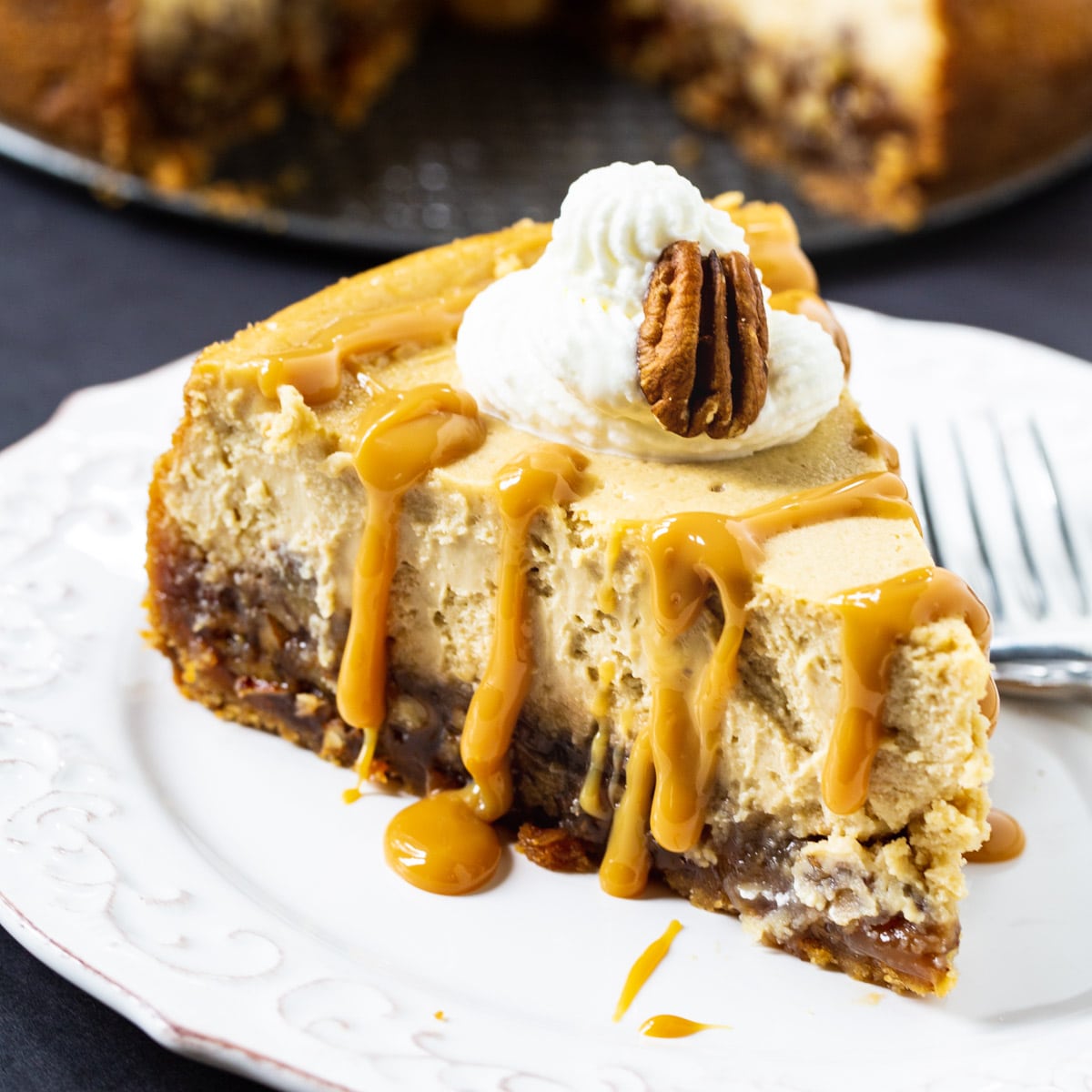 Slice of Pecan Pie Cheesecake topped with whipped cream and caramel sauce.