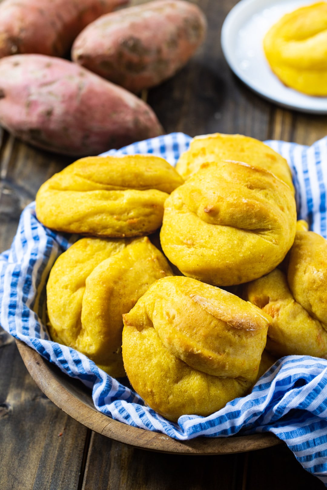 Sweet Potato Rolls in a basket with whole sweet potatoes in background.