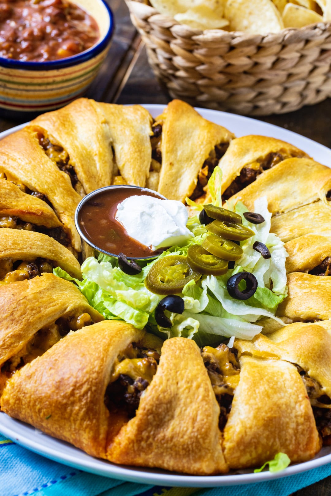 Taco Ring on a plate topped with lettuce, olives and salsa.