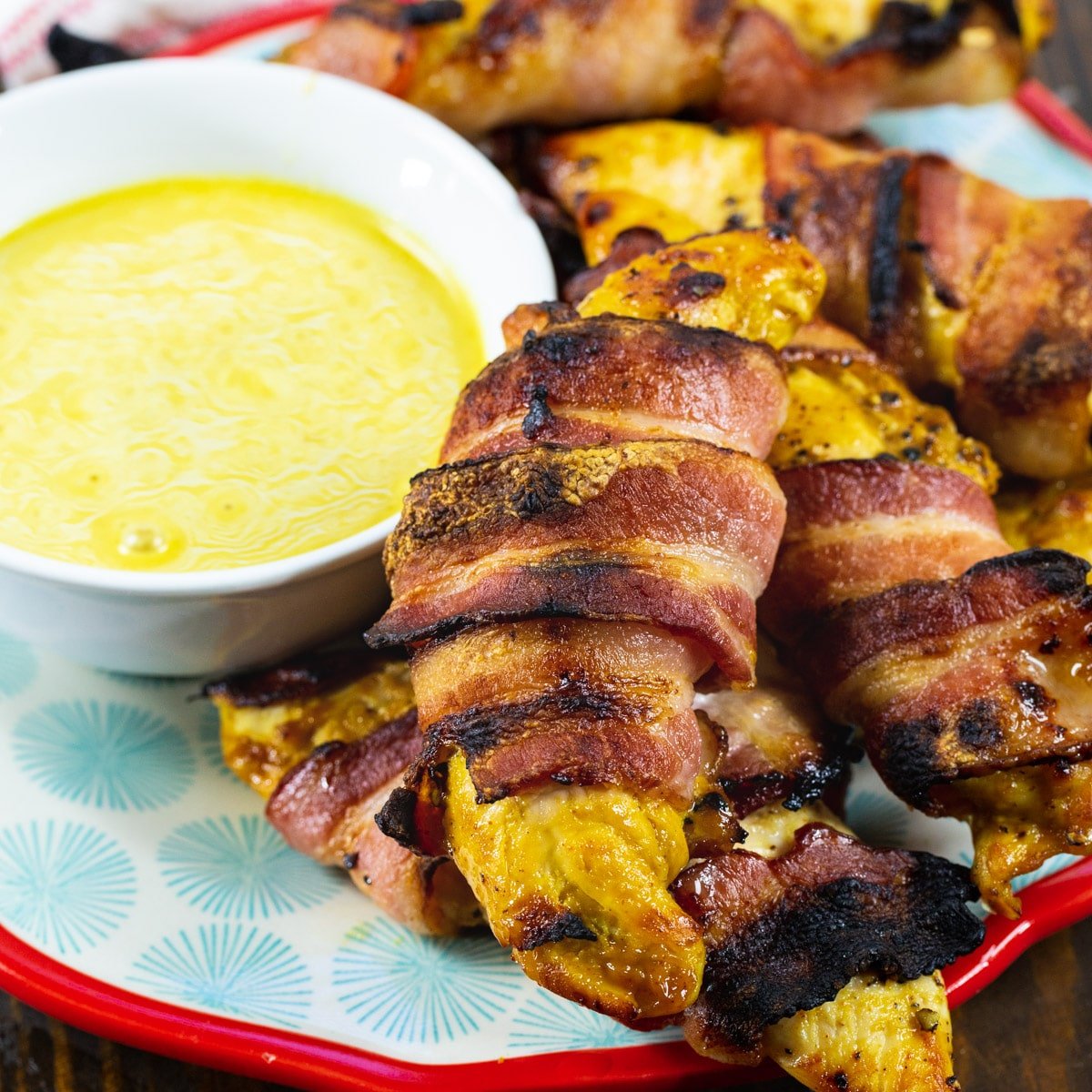 Bacon-Wrapped Honey Mustard Tenders on a plate with a bowl of honey mustard.