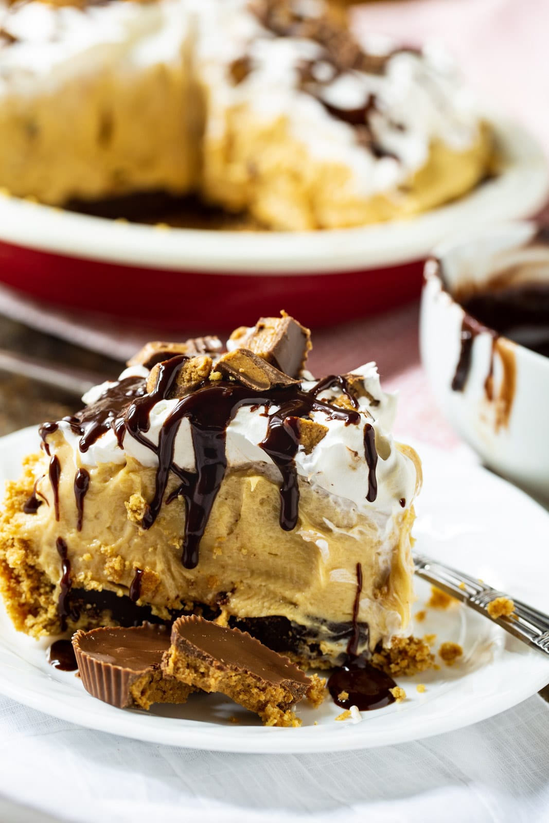 Slice of Peanut Butter Pie on plate with rest of pie in background.