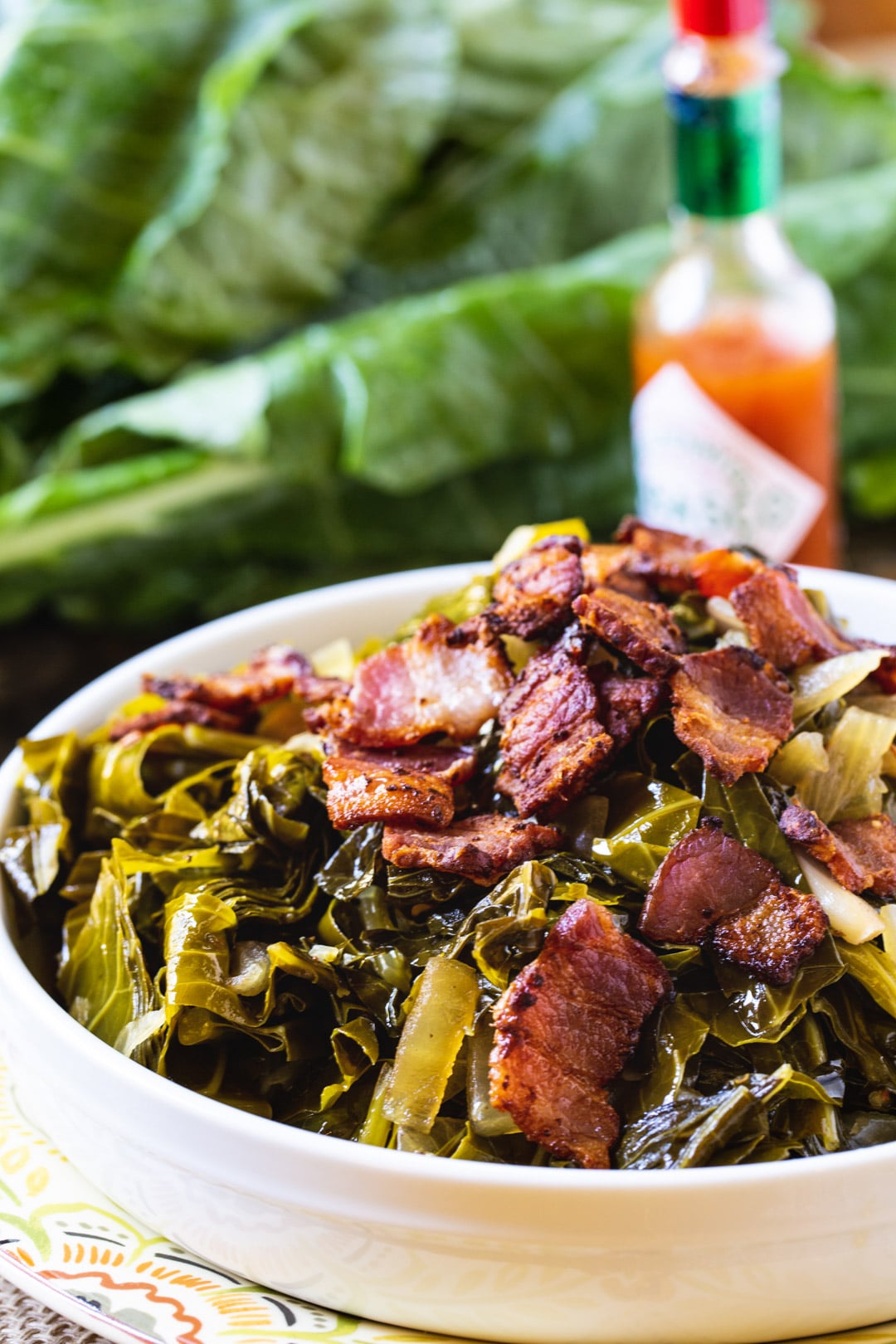 Collard greens topped with bacon in white bowl.