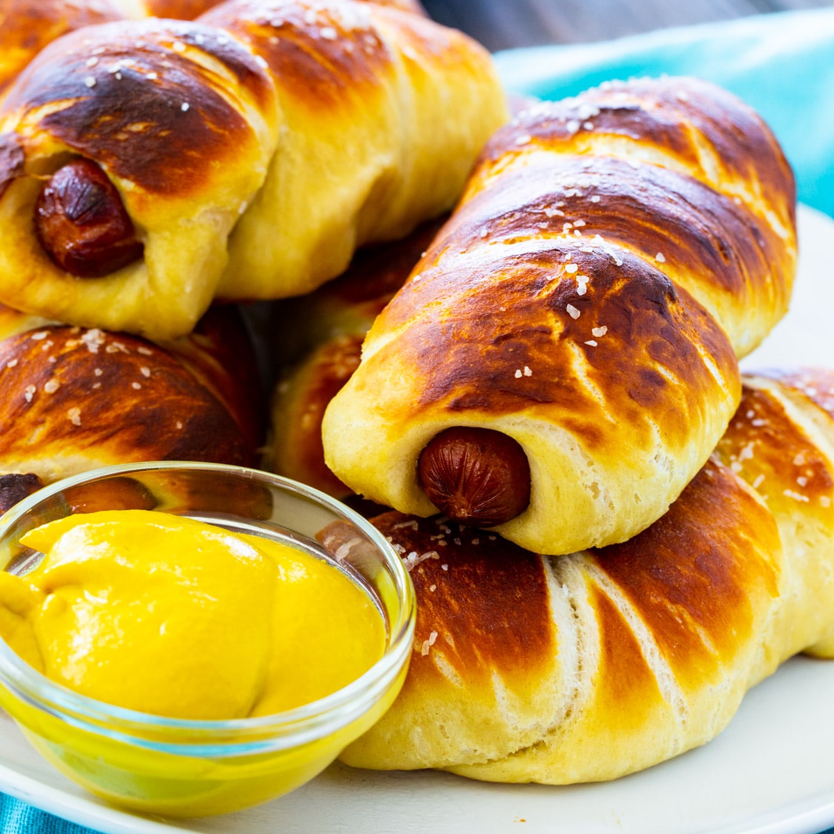 Pretzel Dogs piled on a plate with a small bowl of mustard.
