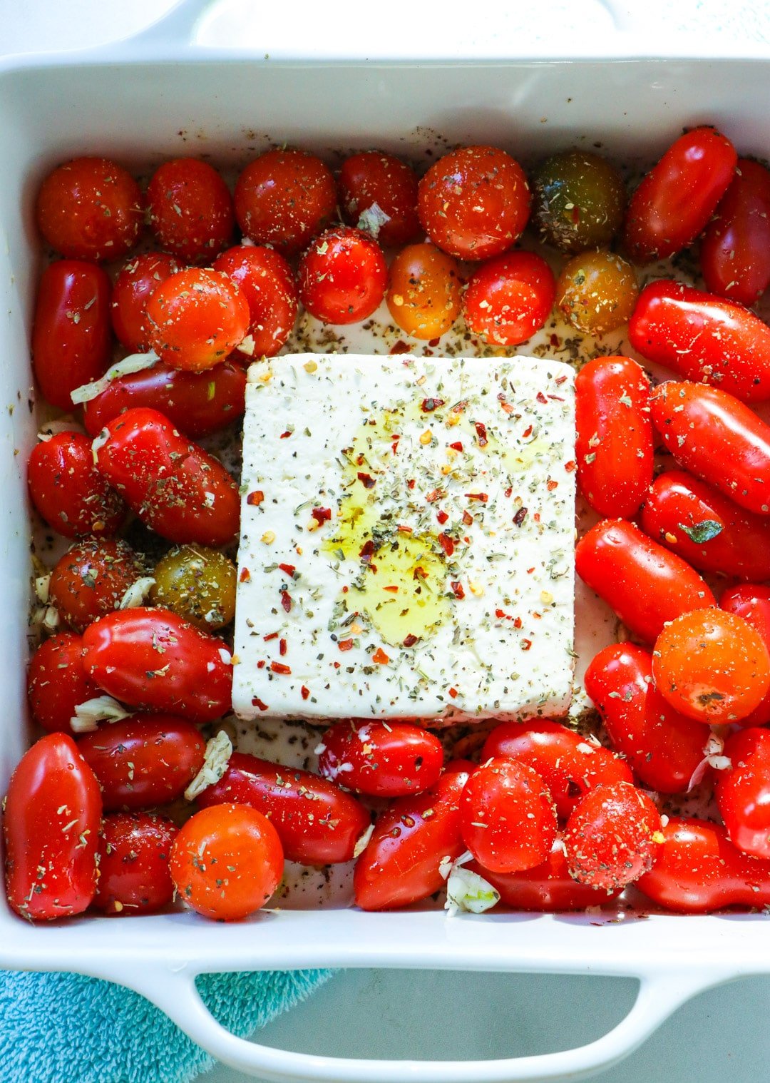 Tomatoes and block of feta in square baking dish.