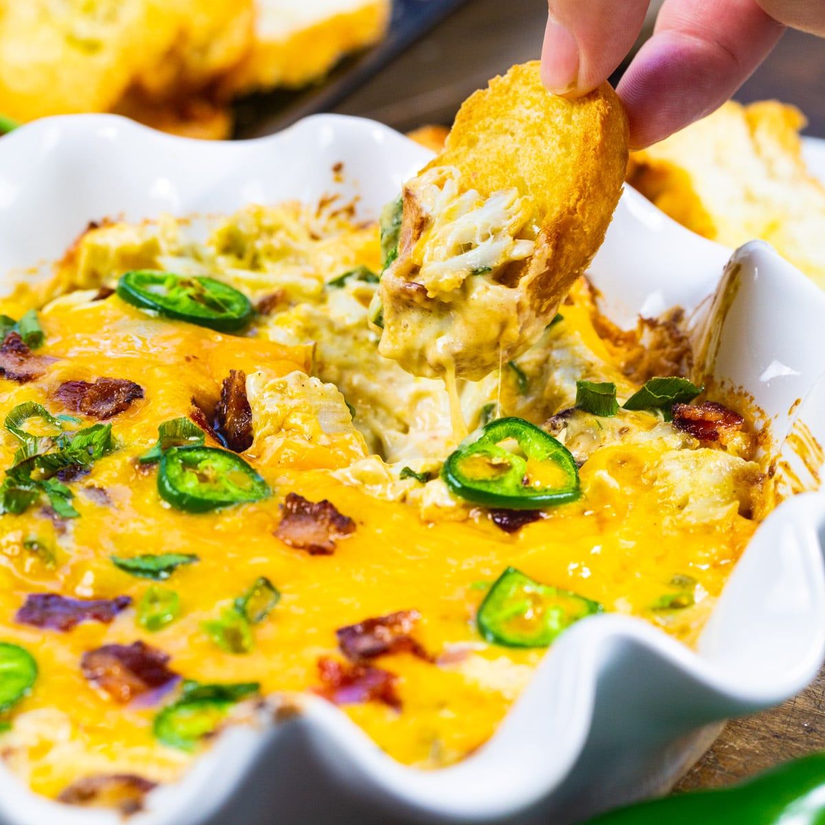 Jalapeno Popper Crab Dip getting scooped up with piece of toasted baguette.