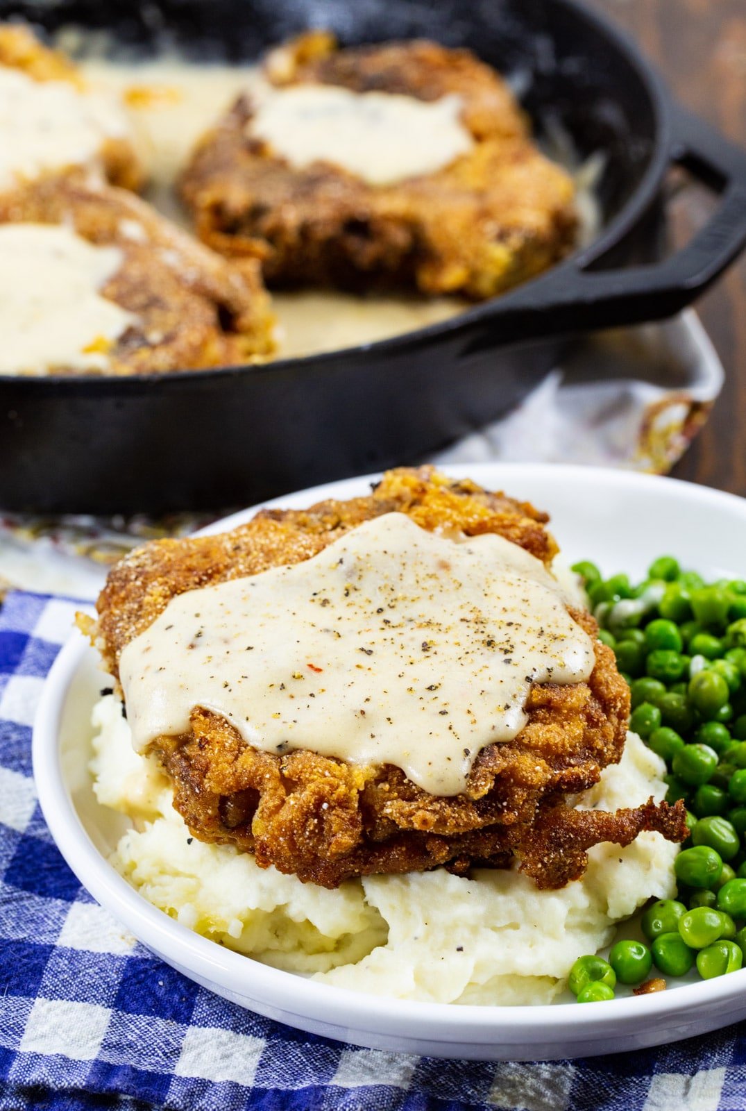 Southern Fried Pork Chop with White Gravy on a plate with mashed potatoes and peas.