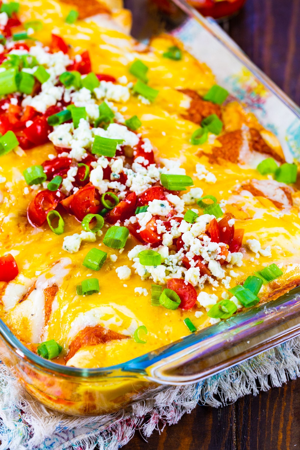 Buffalo Chicken Enchiladas in baking dish topped with tomatoes and blue cheese cumbles.