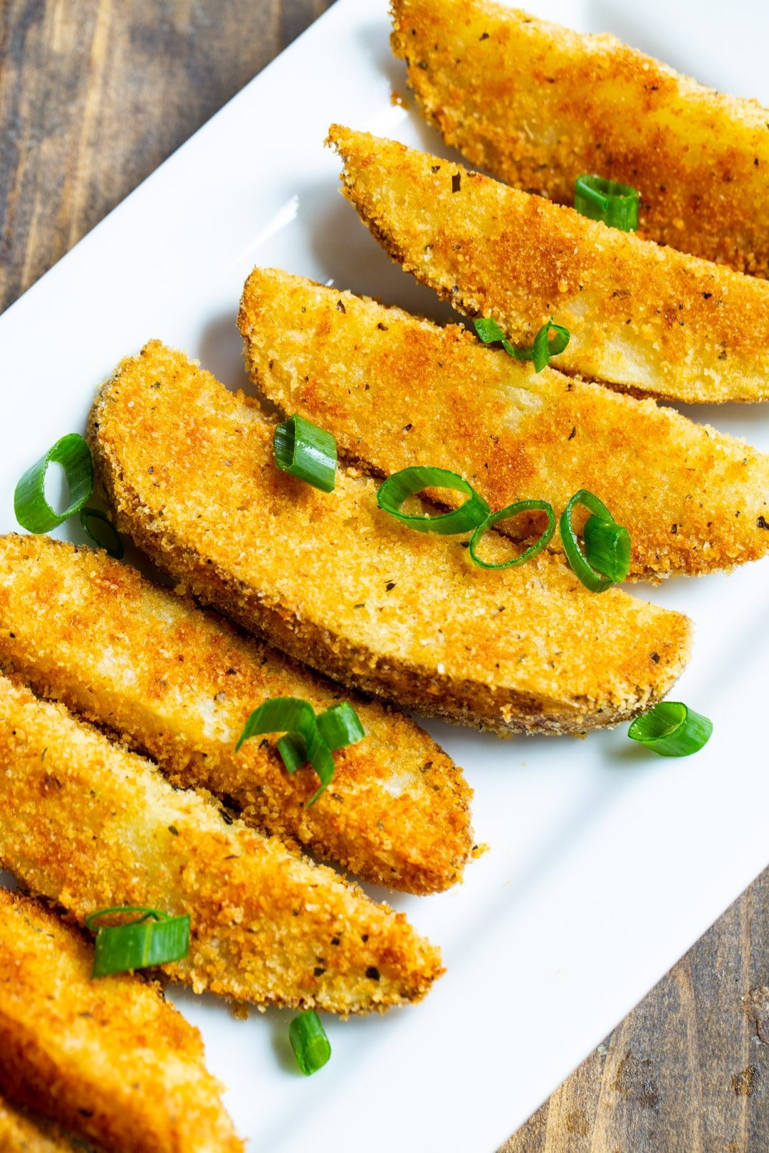 Parmesan Crusted Ranch Potato Wedges on serving plate with green onion slices.