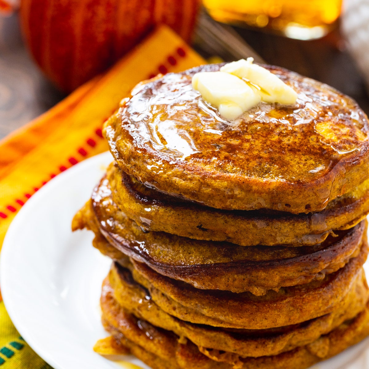Stack of pumpkin pancakes topped with butter and maple syrup.