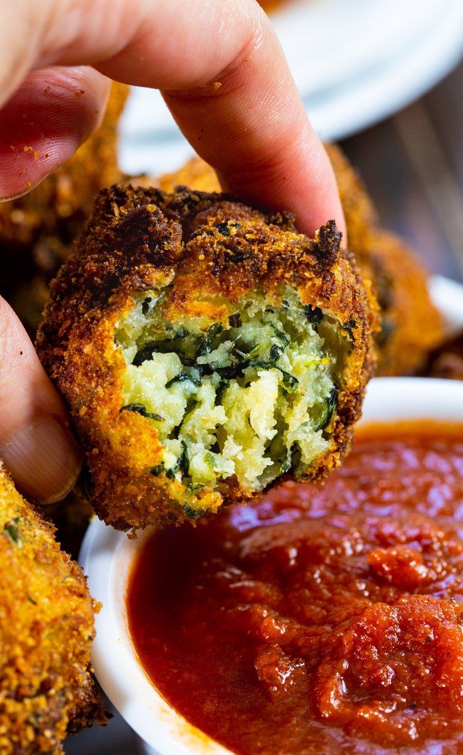 Hand dipping spinach ball in pizza sauce.
