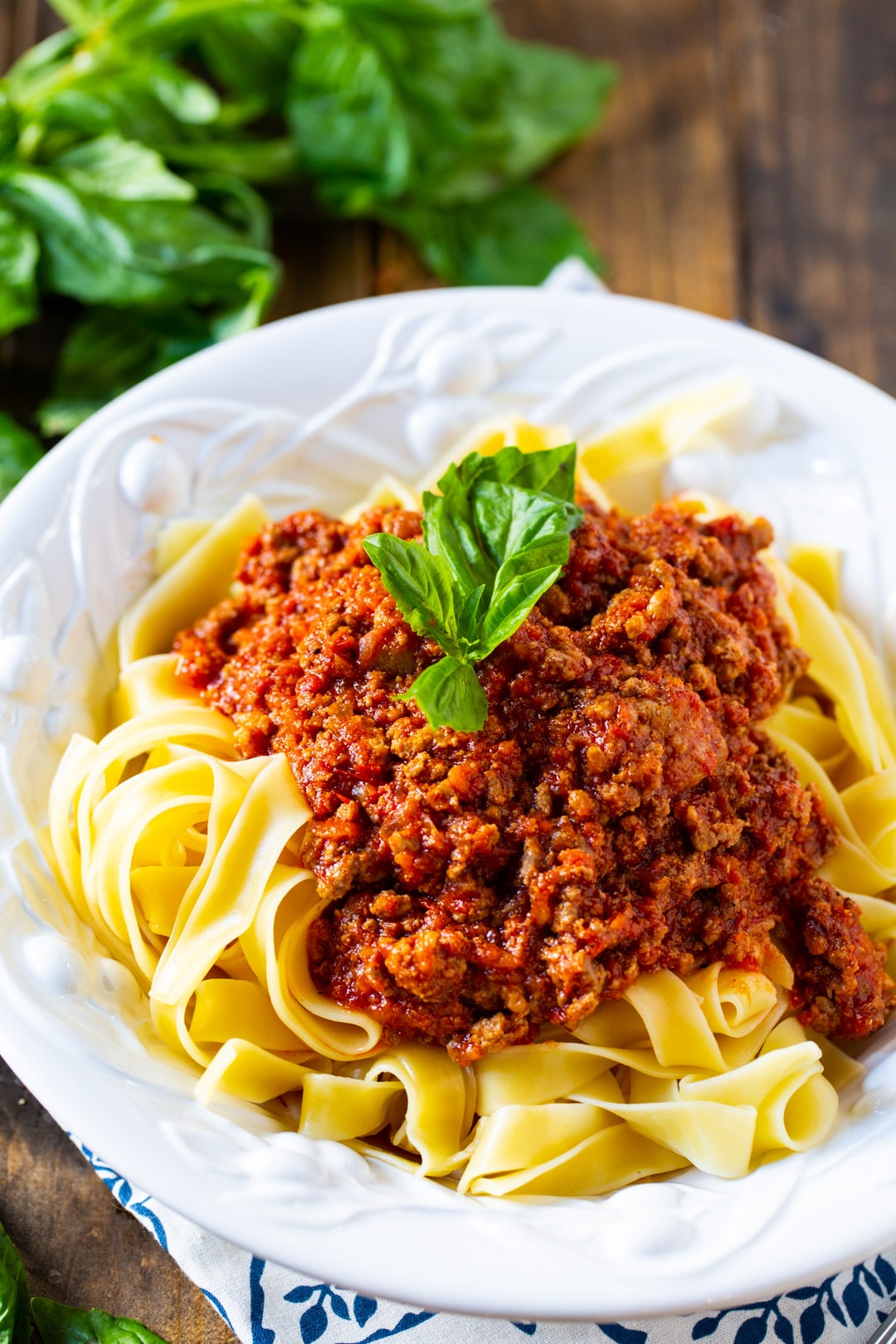 Pappardelle with Bolognese Sauce in bowl with fresh basil in background.