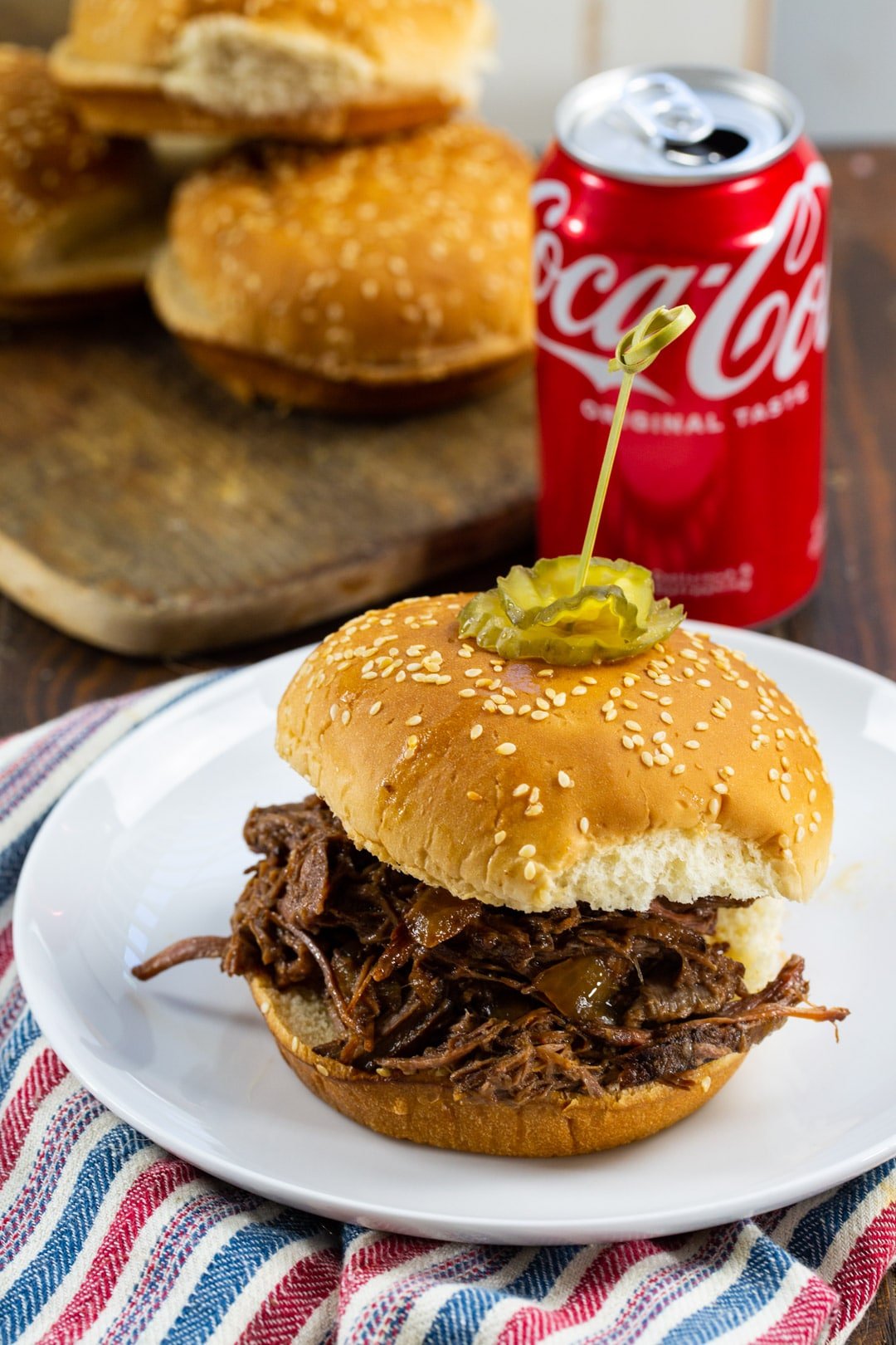 Slow Cooker BBQ Beef on a bun with can of Coke in background.
