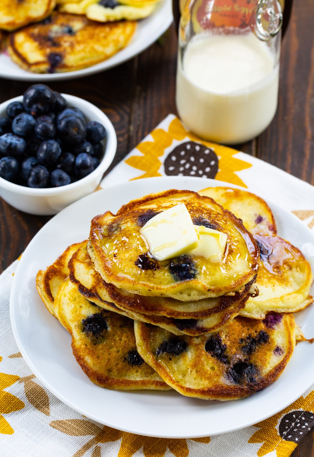 Pancakes on a plate, bowl of blueberries, and jug of milk.