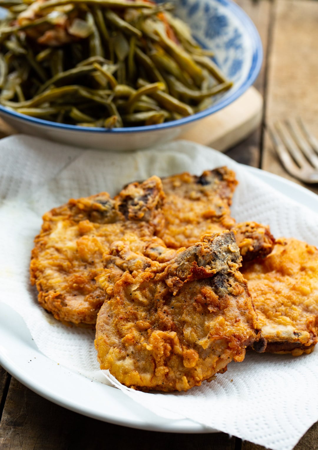 Fried pork chops on a plate and bowl of green beans.