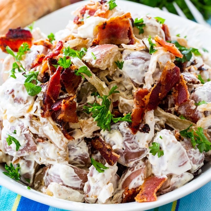 Caramelized Onion Potato Salad topped with crumbled bacon in a serving bowl.