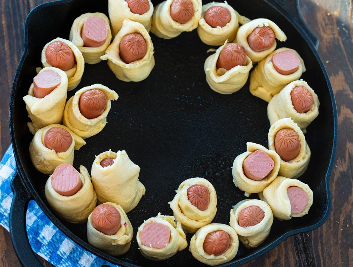 Hot dog pieces wrapped in dough arranged atound edge of skillet.