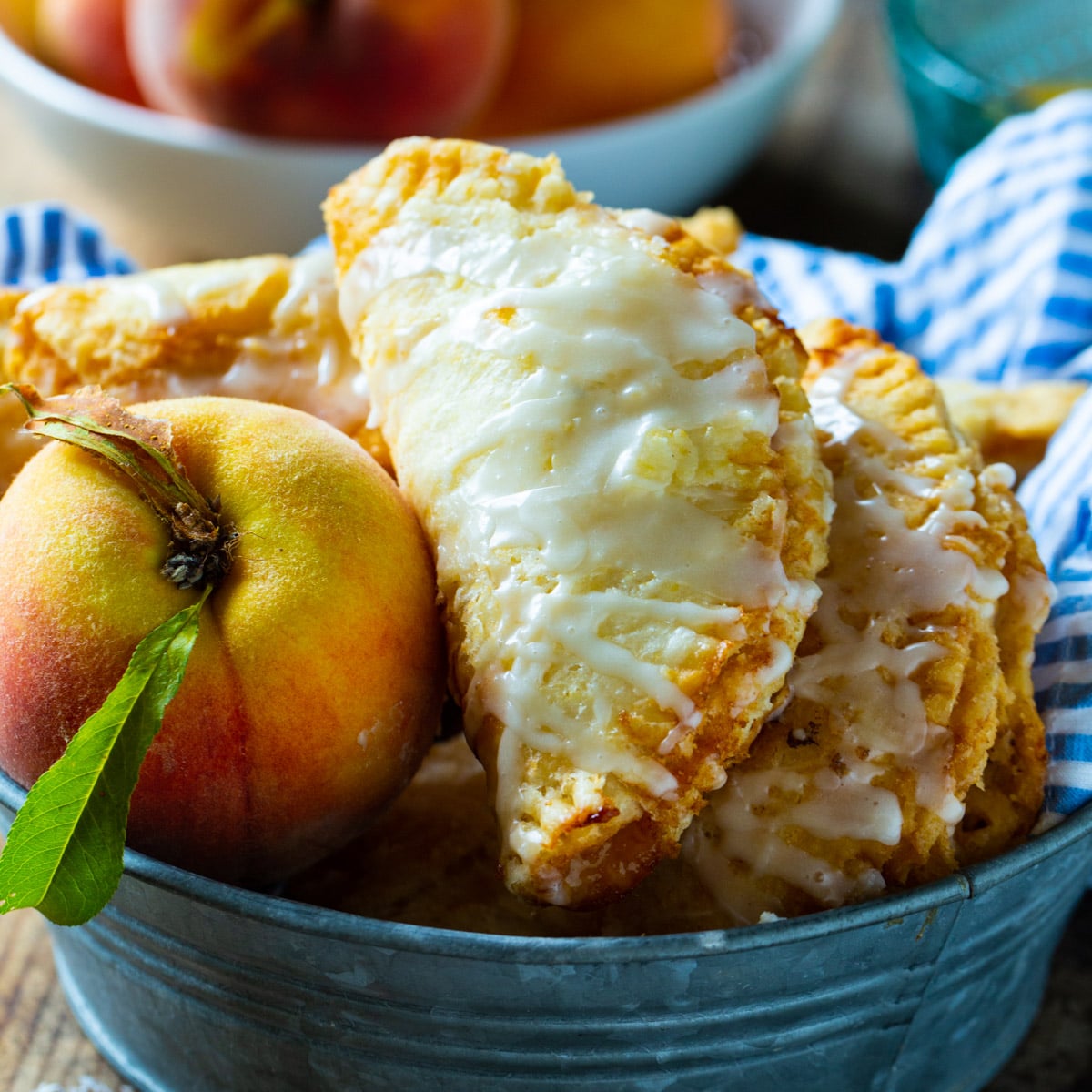 Fried Peach Pies in a metal tin with a fresh peach.