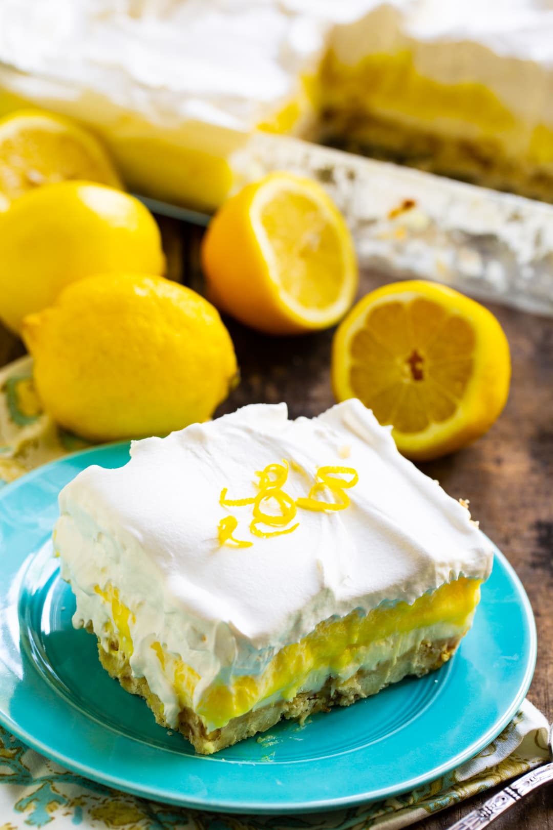 Lemon Lush slice on a small plate with fresh lemons in background.