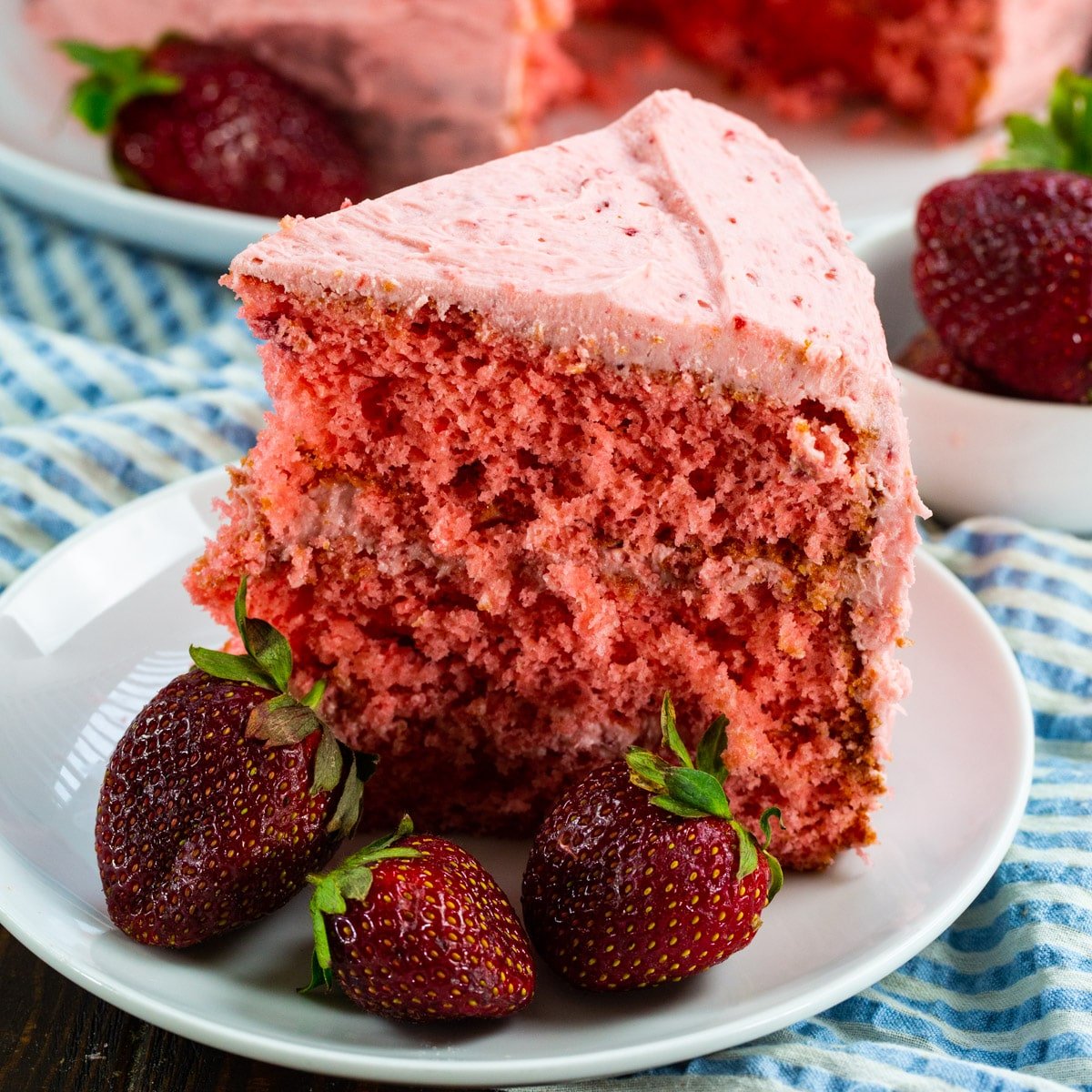 Slice of Strawberry Layer Cake on a plate with fresh strawberries.