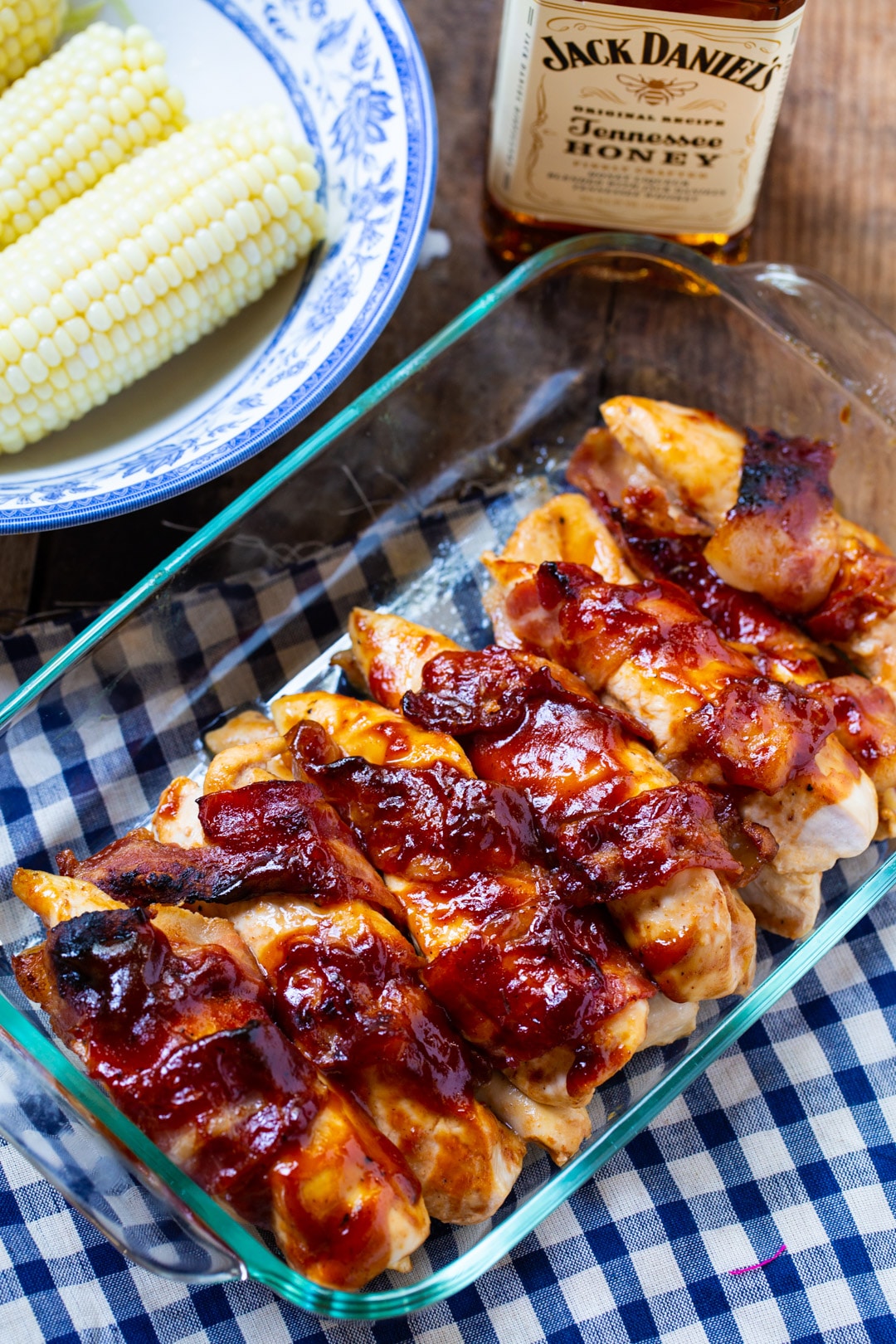 Cooked BBQ Chicken in a 9x13-inch baking dish, bowl of corn, and bottle of bourbon.