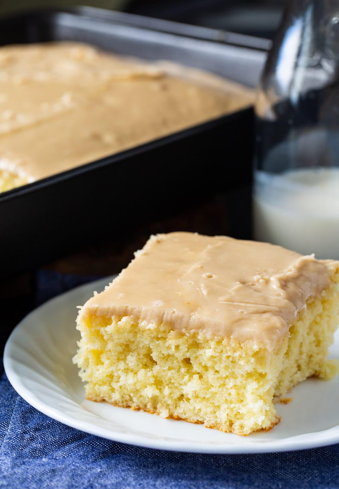 Slice of cake on a plate with rest of sheet cake in background.