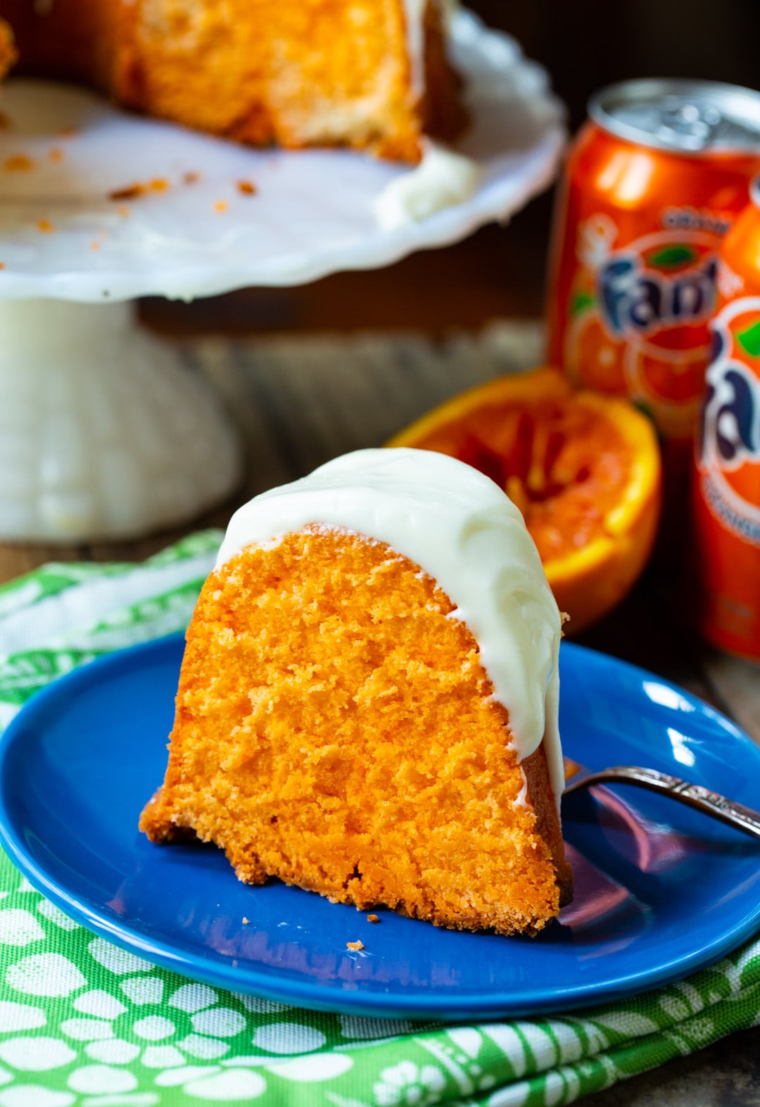 Slice of pound cake on a blue plate and cans of Fanta in background.