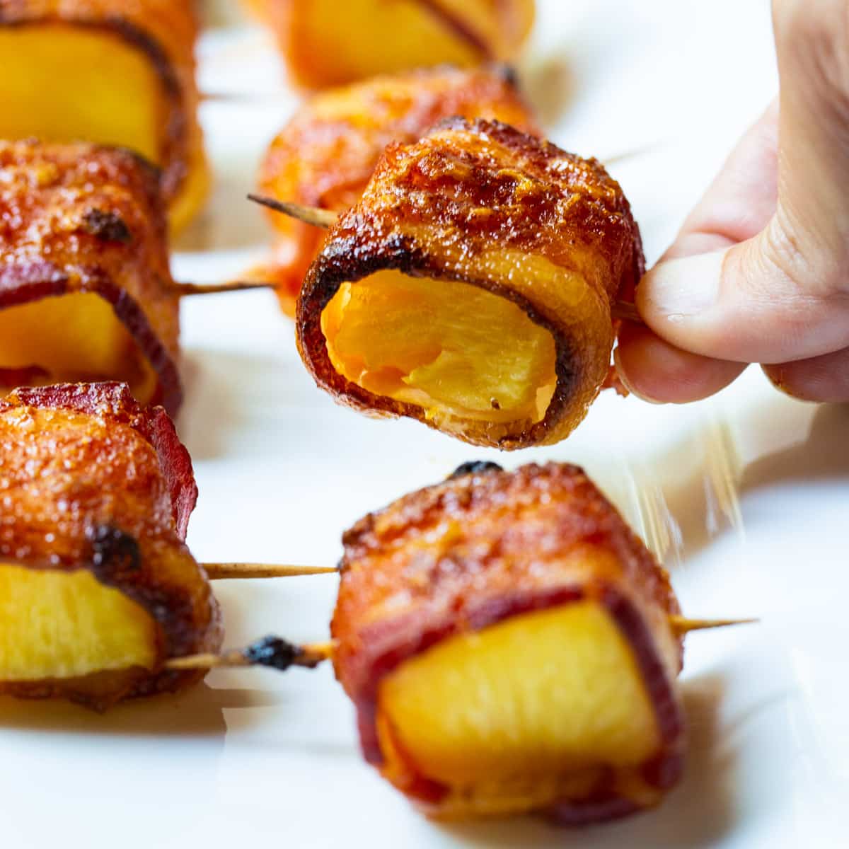 Hand picking up a Spicy Bacon Wrapped Pineapple Bite.