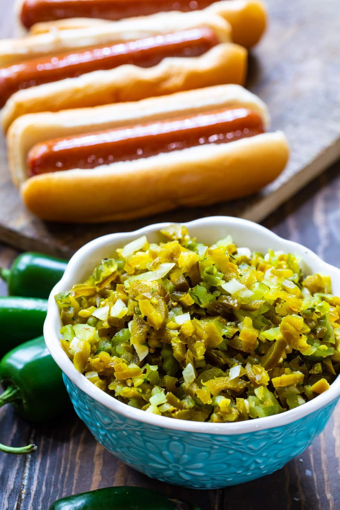 Relish in a bowl and hot dogs in background.