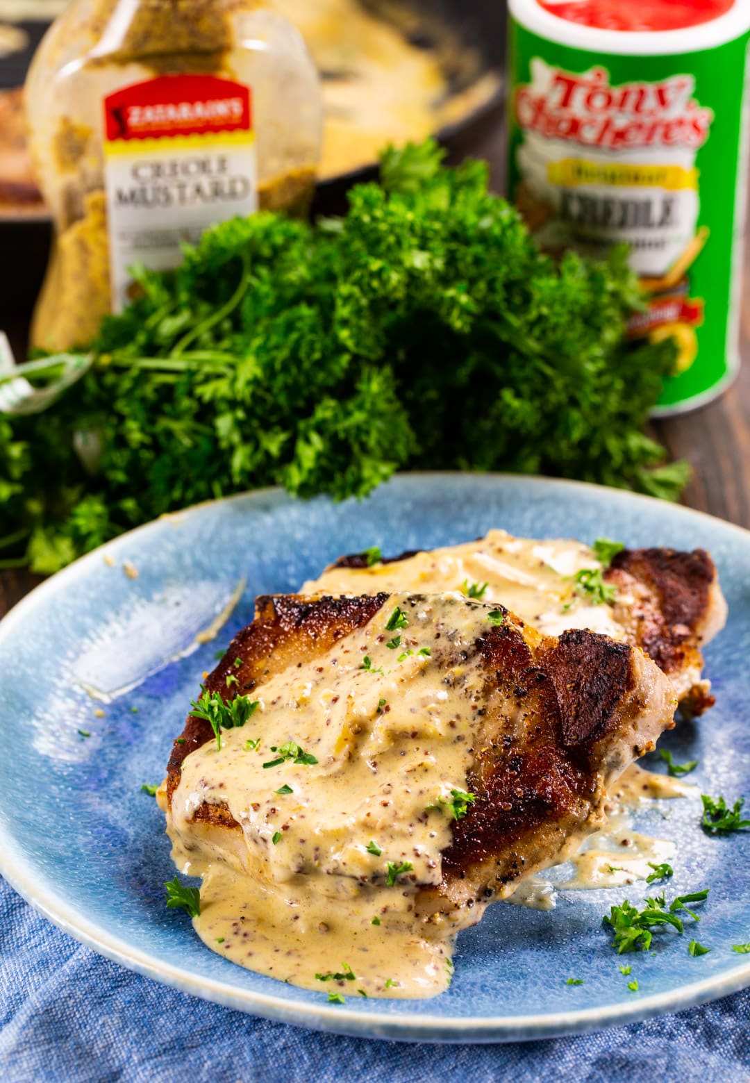 Two Pork Chops with Creole Mustard Sauce on a plate with fresh parsley in background.