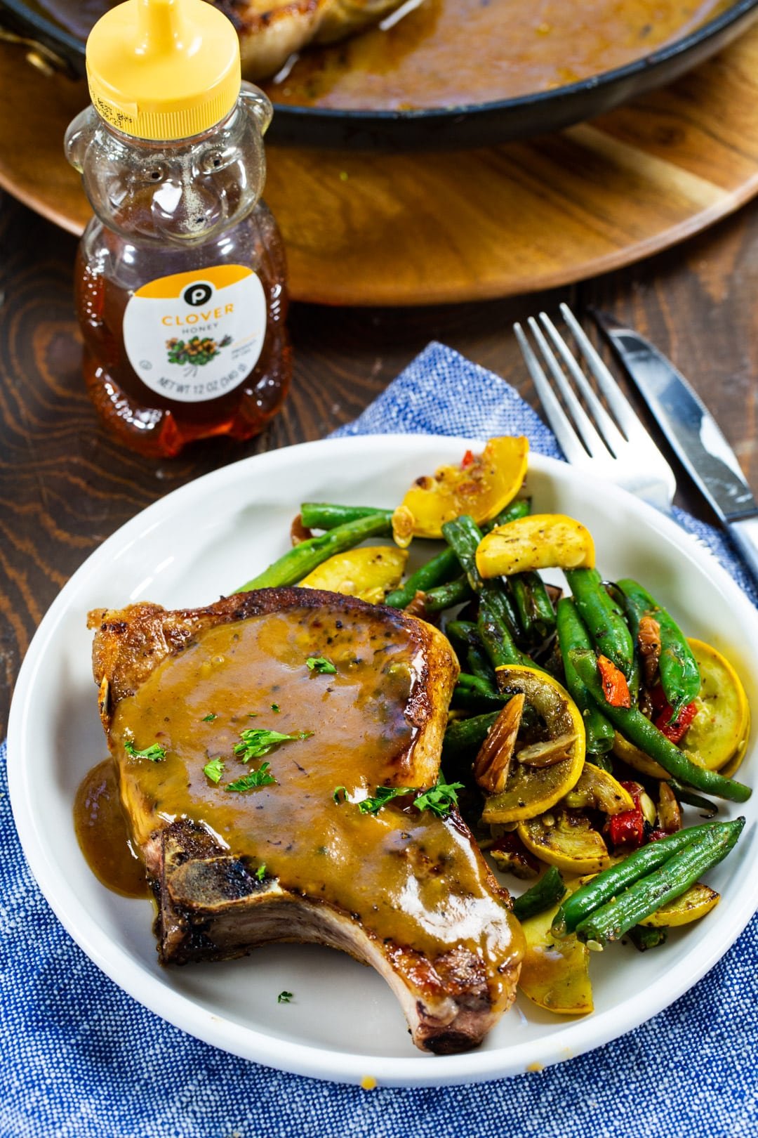 Honey Mustard Pork Chop on plate with green beans and squash and a bottle of honey.