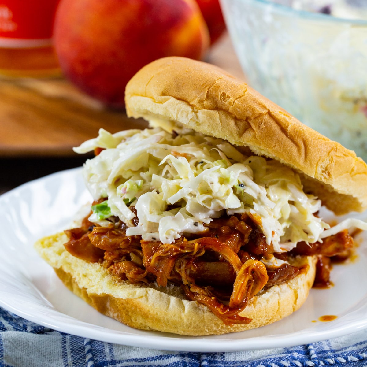 Slow Cooker BBQ Peach Pulled Chicken on a bun with coleslaw.