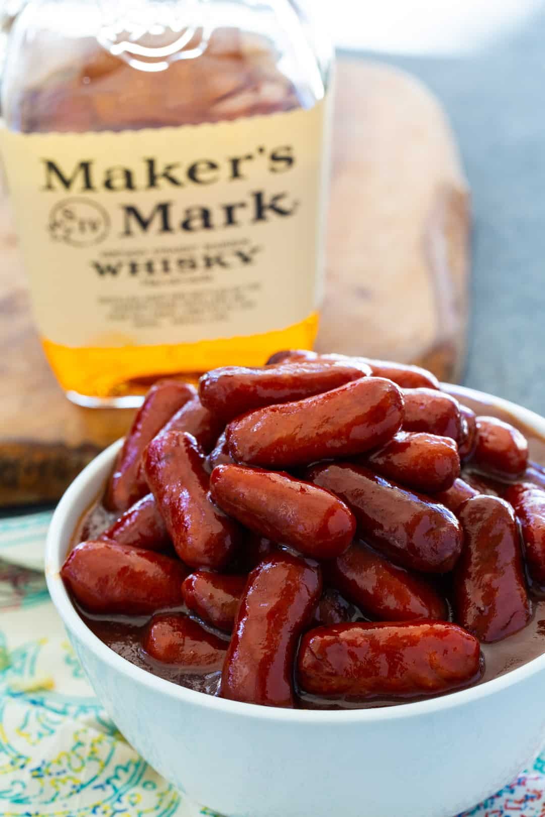 Crock Pot Bourbon Smokies in a bowl and bottle of bourbon.