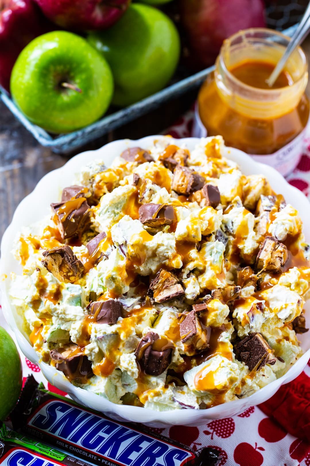 Apple Salad in a bowl surrounded by whole apples and snickers bars.