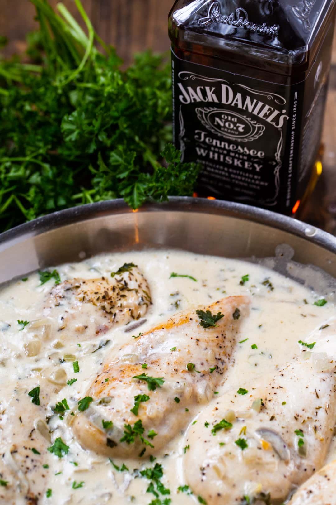Chicken and creamy sauce in skillet and bottle of Jack Daniels.