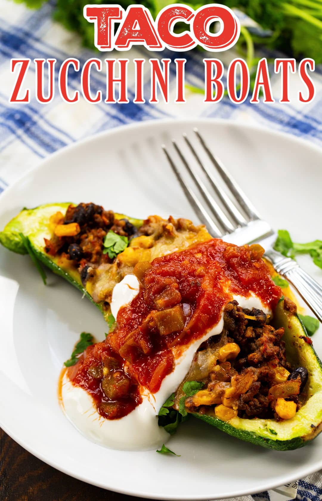 Taco Zucchini Boat topped with sour cream and salsa on a plate.
