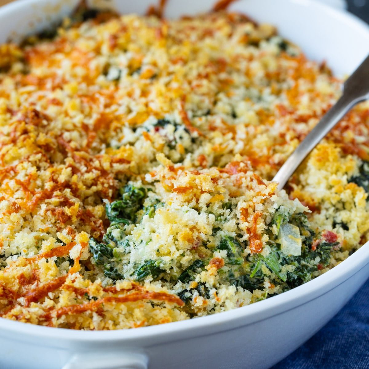 Spoon scooping Pimento Cheese Creamed Spinach out of baking dish.