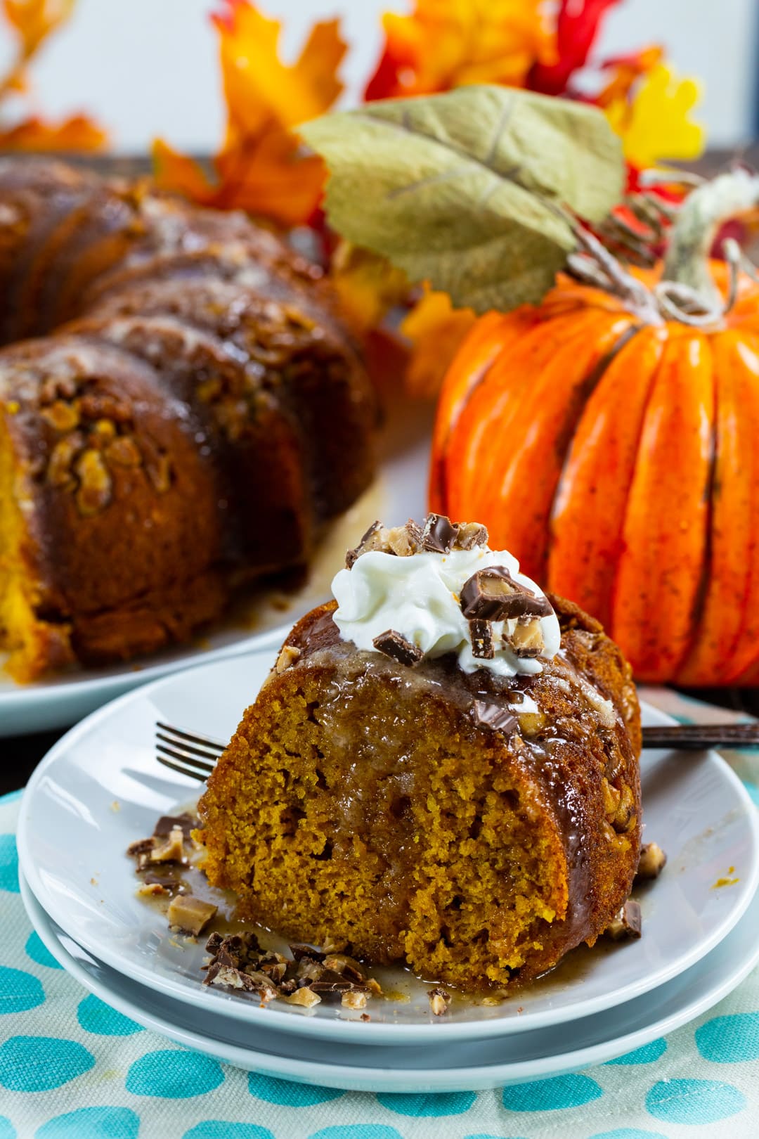 Piece of cake on a plate with pumpkin and rest of cake in background.